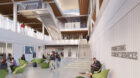 Students sit in atrium with green chairs. Stairs lead up three storeys.