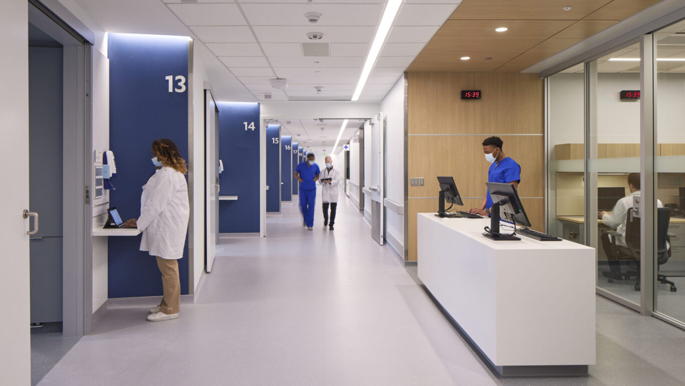 Slide 1 of 7, Interior view of nurse station and inpatient care corridor.