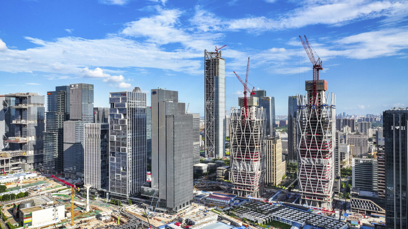 Slide 1 of 1, Construction image of 2 towers with a defined diamond grid structure toping out in the city of Guangzhou.