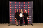 Award recipients stand backstage with award certificate in front of AIA Chicago backdrop