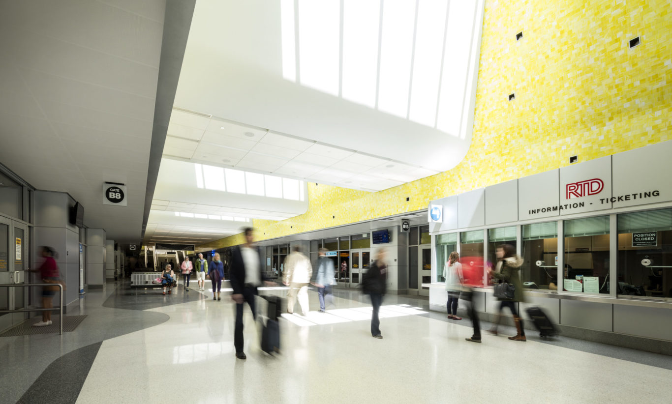 Slide 3 of 7, Underground, a 22-gate bus concourse services 16 regional, express, and local bus routes. The terminal, measuring 980 feet in length, serves a dual purpose as a pedestrian concourse that connects the constellation of transportation programs distributed across the site. Vivid colors and natural lighting help passengers orient themselves while handsome terrazzo floors and sparkling yellow glass tilework elevate the ambience of terminal beyond the often-unimaginative bus depot experience. A series of skylights and glass pavilions flood the hall with daylight, infusing the station with a sense of motion and spaciousness. One of the largest projects of its kind in the United States, the redevelopment of the former rail yards at Denver Union Station is a case study of the power of transit-oriented urban design. This substantial public investment has catalyzed an unprecedented wave of private-sector activity. Sensitive to its historic location, but fundamentally forward looking in its technical sophistication and city-building spirit, Denver Union Station sets the standard for 21st-century intermodal hubs.